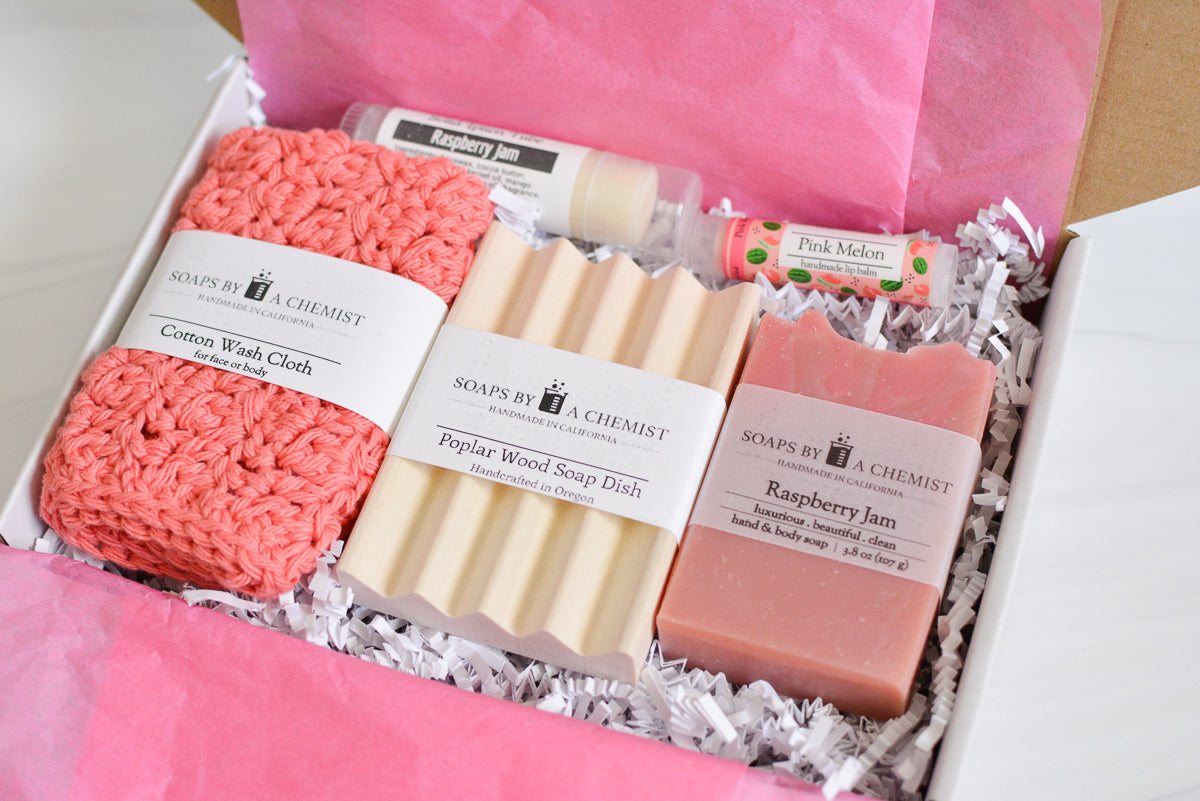 pink side view of mother's day gift set with handmade ocean soap, ceramic soap dish, cotton crocheted wash cloth, lip balm, and solid lotion tube.