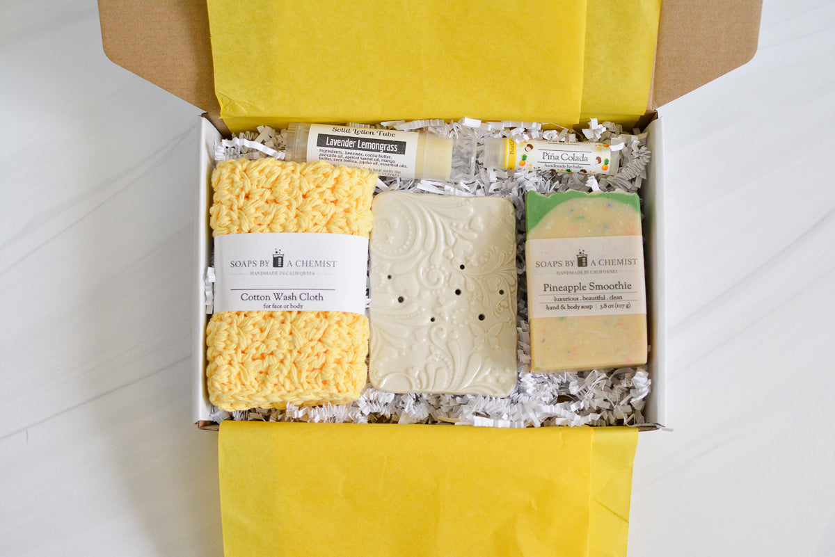yellow mother's day gift set with handmade ocean soap, ceramic soap dish, cotton crocheted wash cloth, lip balm, and solid lotion tube. top view