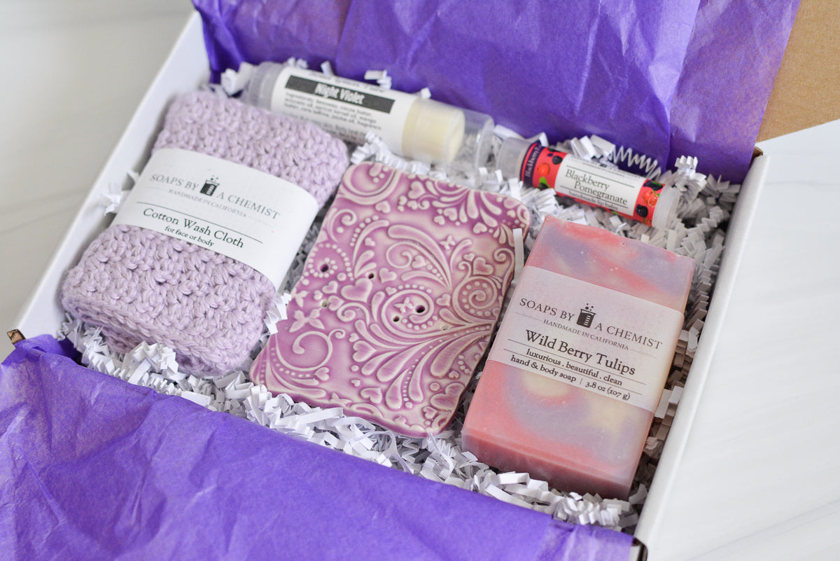 purple mother's day gift set with handmade ocean soap, ceramic soap dish, cotton crocheted wash cloth, lip balm, and solid lotion tube. diagonal view close up