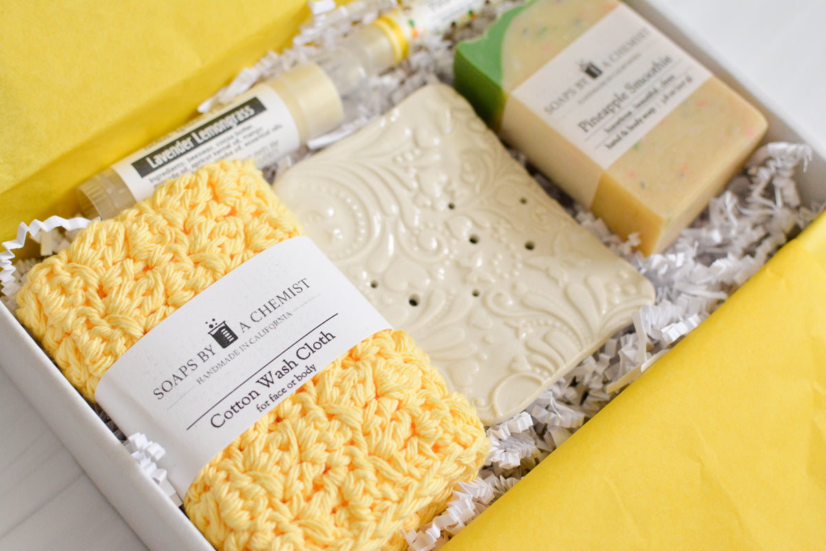 yellow mother's day gift set with handmade ocean soap, ceramic soap dish, cotton crocheted wash cloth, lip balm, and solid lotion tube. close up